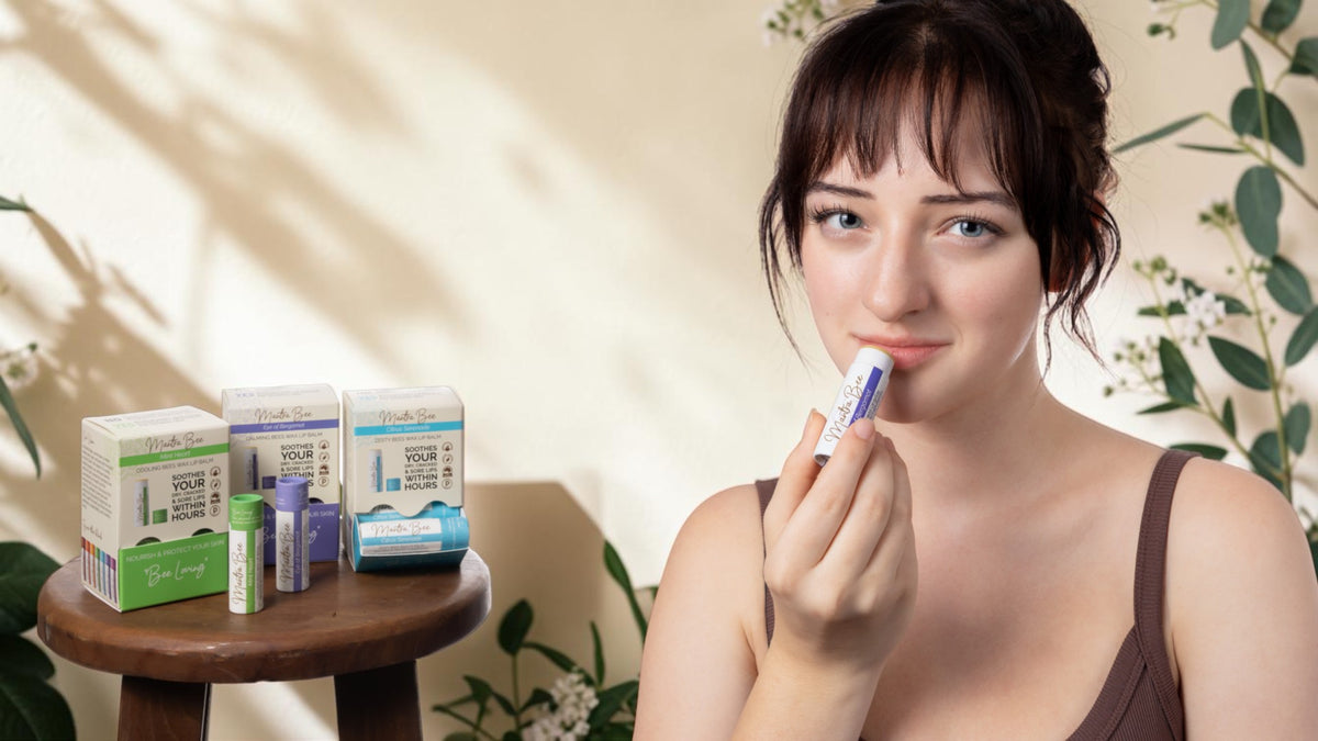 Woman applying Mantra Bee natural beeswax lip balm beside plastic-free lip balm display boxes