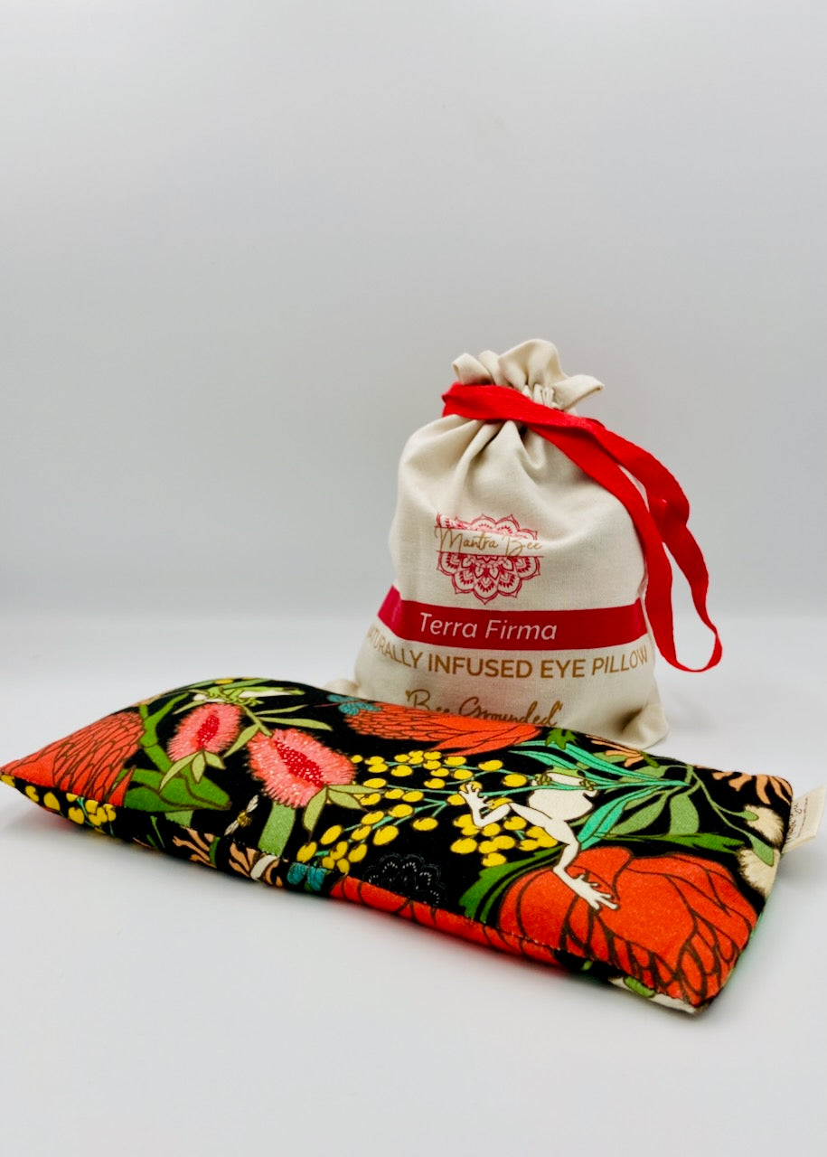 Decorative eye pillow with green tree frogs and floral design and a drawstring bag labeled 'Terra Firma' on a light gray background.